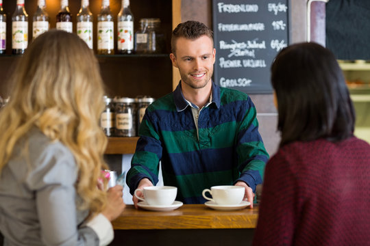 Bartender Serving Coffee To Female Friends At Cafe