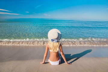 Fototapeta na wymiar Cute blonde woman in white bikini on sea sand beach