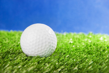 Golf ball on green field grass against blue sky