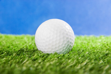 Golf ball on green field grass against blue sky