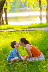Fototapeta premium Mom and son woman child sitting on grass kissing sunset Roma