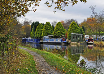Beautiful English canal scene with colourful barges flanked by attractive trees in pretty Crooke...