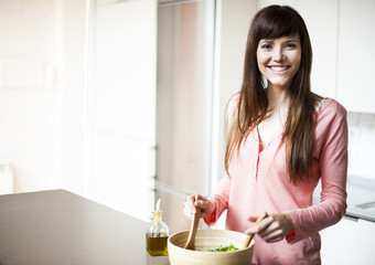 Portrait of young happy woman making salad at domestic kitchen