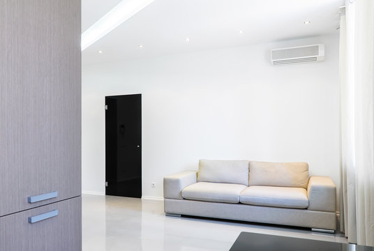 A soft settee in a luminous white room. A black door is closed.