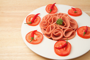 Slices of ham on white  plate with tomato and chili