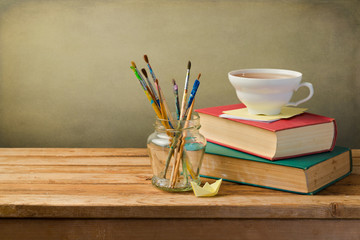 Vintage books, cup of tea and painting brushes on wooden table
