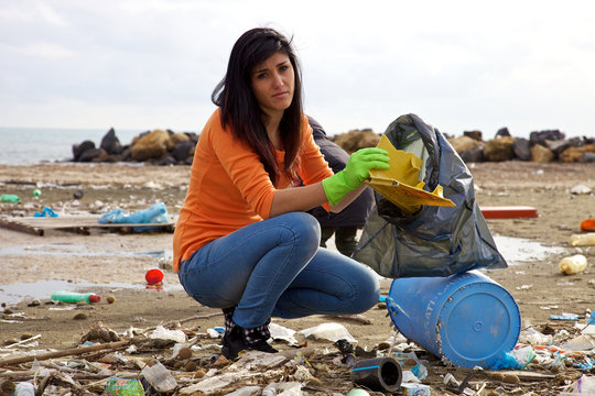 Young woman trying to clean dirty beach ecological disaster