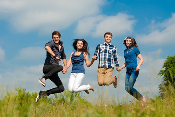 Four happy teenage friends jumping high in blue sky