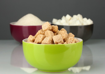 Bowls with different types of sugar on a gray background