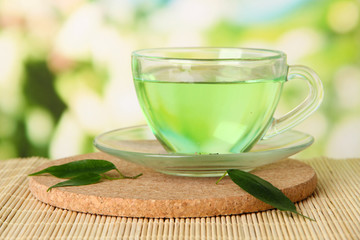 Transparent cup of green tea on bamboo mat, on nature