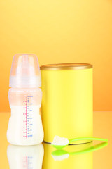 Bottle with milk and food for babies on orange background