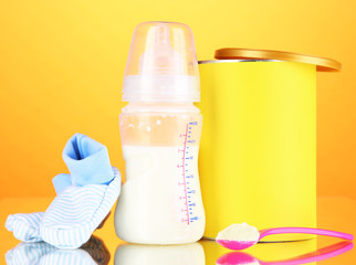 Bottle with milk and food for babies on orange background