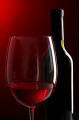 Glass of wine with bottle on bright red background