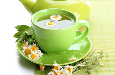 Cup and teapot of herbal tea with wild camomiles and mint,