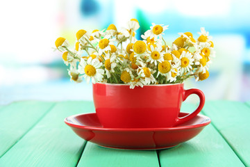 Bouquet of chamomile flowers in cup, on bright background