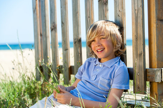 Happy Boy Sitting Next To Fence On Beach.