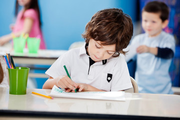 Boy Drawing With Sketch Pen At Desk In Kindergarten