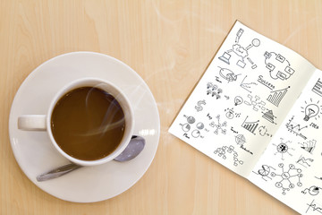 Cup of hot coffee and  book with graph on wood table