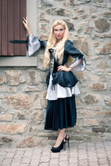 Beautiful girl wearing a medieval dress. Stone wall background. 