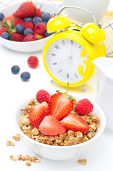 Breakfast - granola with fresh berries, milk, yellow alarm clock