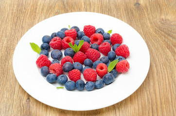 Fresh raspberries and blueberries on a plate on a wooden table