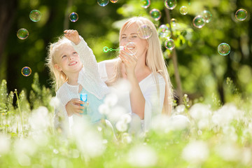 Happy mother and daughter blowing bubbles in the park