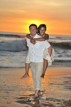Bride and groom walking barefoot on Bali beach at sunset
