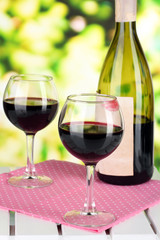 Two glasses of wine and bottle on table on nature background