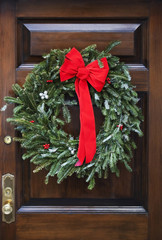 Wooden front door decorated with writh and red bow.