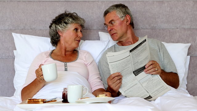 Husband reading the newspaper to his wife during breakfast