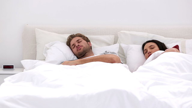 Couple sleeping peacfully with partner pressing snooze