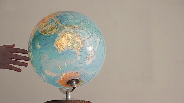 Geography teacher's hand turns an illuminated globe