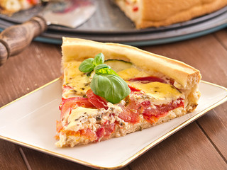 Quiche aus Tomaten und Zucchini auf einem Holztablett.
