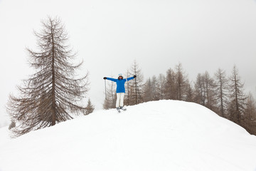 Naklejka na ściany i meble Happy ski woman standing in snow with pine trees.