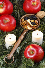 Dried fruits on fir branches among red ripe apples and candles.
