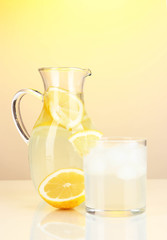 Lemonade in pitcher and glass on yellow background