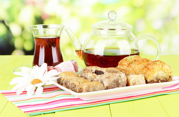 Sweet baklava on plate with tea on table on bright background