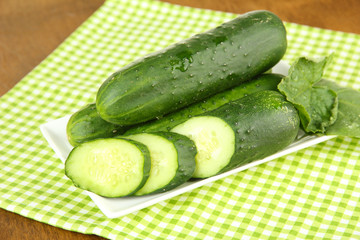 Tasty green cucumbers on color napkin, on wooden background
