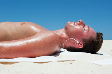 Naklejka premium Man sunbathes and listens to music on the beautiful beach