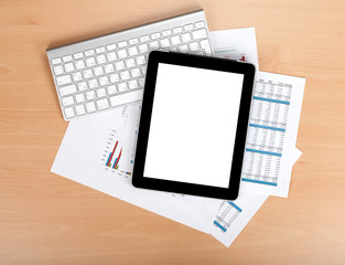 Tablet with blank screen over papers with numbers and charts