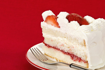 Slice of homemade strawberry cream cake against red background