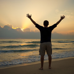 Fototapeta premium Man with his hands up on the dawn on the beach