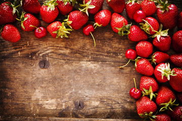 Strawberry and cherry on the old brown wooden background.