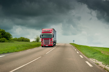 Red truck on highway over stormy sky on background