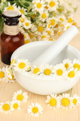 Fototapeta na wymiar Essential oil and chamomile flowers in mortar on wooden table