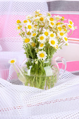 Many chamomile in glass teapot on light cloth background