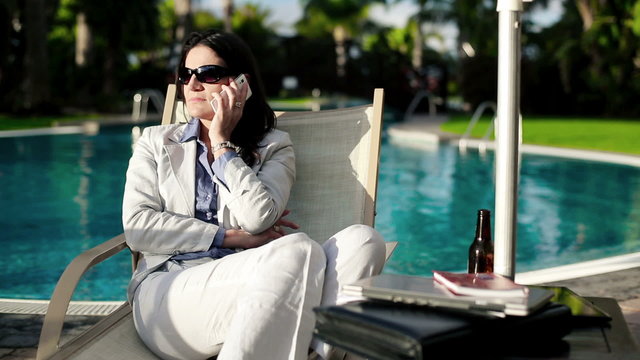 Businesswoman sitting by the poolside and getting bed news by ce