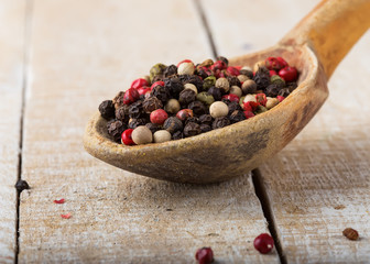 Mixed pepper in old spoon  on wooden background