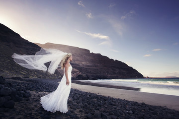 A bride standing in the ocean, the veil fluttering in the wind.