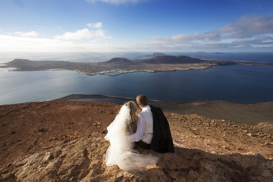 Bride and groom sitting on a volcanic landscape background.